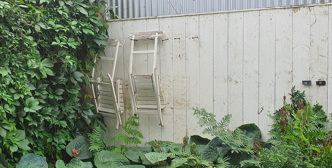 Praktisch und malerisch: Gartenstühle, die an einer Holzwand hängen. © GartenRadio.fm